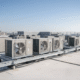 The image depicts a commercial building rooftop featuring several large HVAC rooftop units positioned under a clear blue sky. These commercial HVAC systems are essential for maintaining temperature and energy efficiency in the building, ensuring optimal air quality and comfort for its occupants.